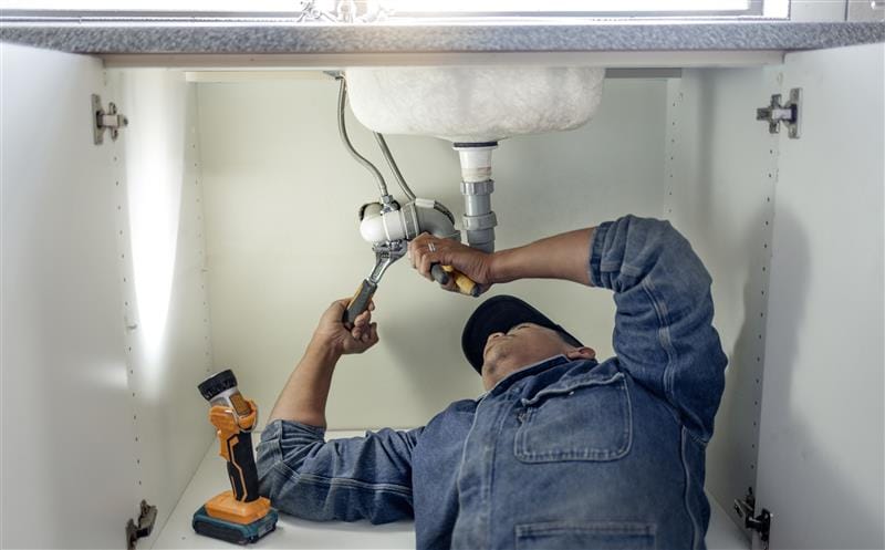 Plumber repairing pipes beneath a bathroom sink in El Monte